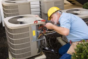 A Pronto technician in a yellow hard hat efficiently repairs wiring on an outdoor AC unit next to a customer's building.