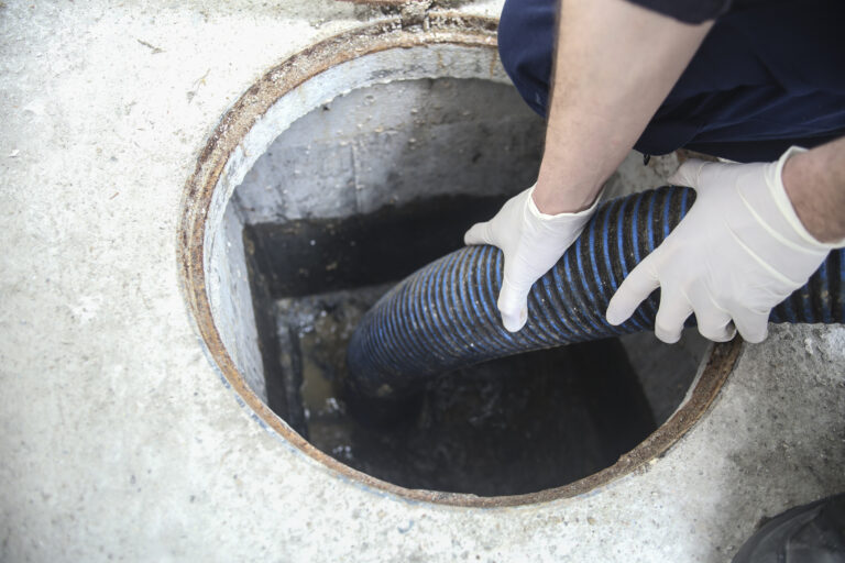 A Pronto Plumbing technician in gloves uses a large hose to service a septic tank through an open concrete access point.