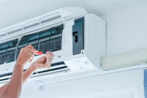 A Pronto technician uses a screwdriver to service a wall-mounted AC unit inside a customer's home.