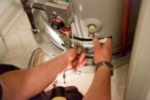 A Pronto Plumbing technician uses a screwdriver to service the lower panel of a customer's water heater.