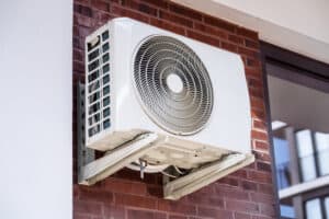 A Pronto team-installed white outdoor AC unit is securely mounted on a brick wall beside a customer’s window.