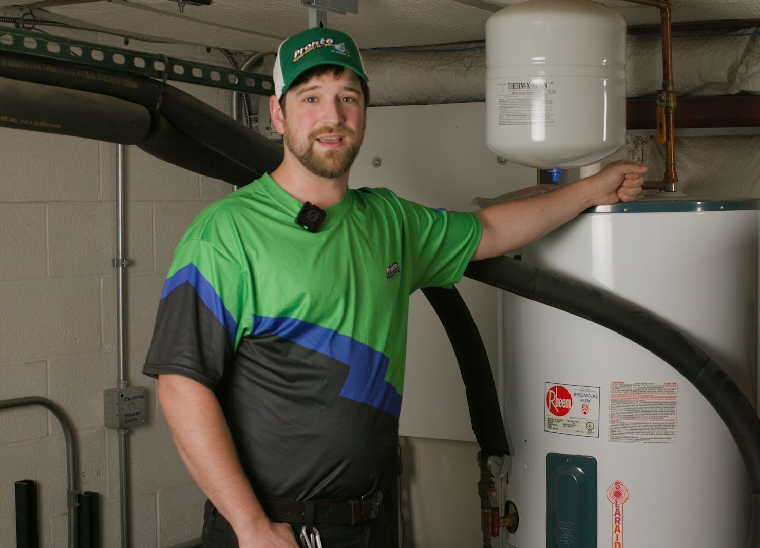 A Pronto Plumbing technician stands by a Rheem water heater in a utility room, smiling and ready to assist with expert service.